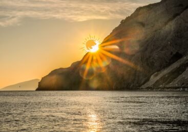 Golden sunset over a Greek island, reflecting on the sea with a dramatic mountain silhouette.