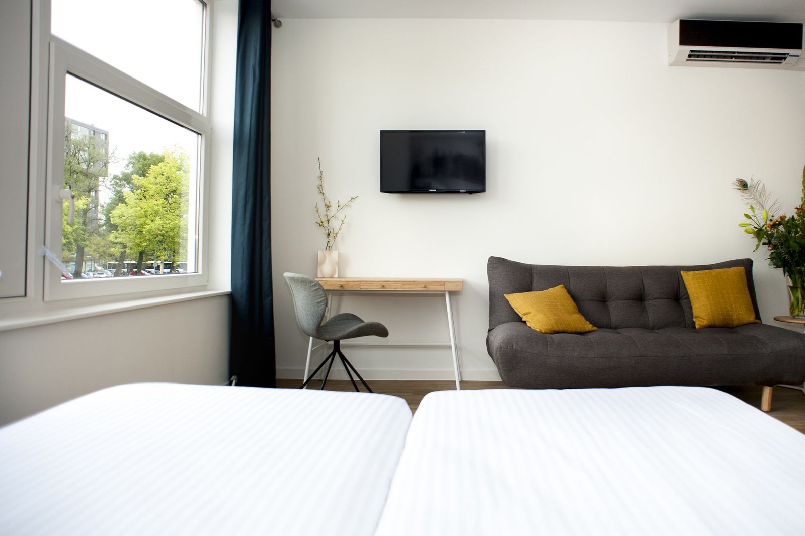 Modern hotel room at i Hotel Amsterdam with a minimalist design, featuring a cozy bed, sofa, desk, and large window overlooking the city