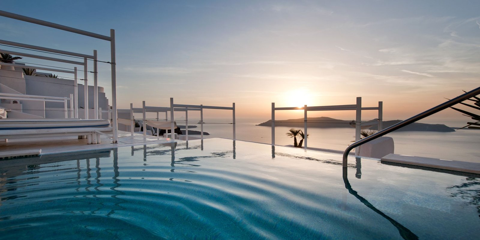Infinity pool overlooking the Santorini caldera at Andromeda Villas Spa Resort during sunset.