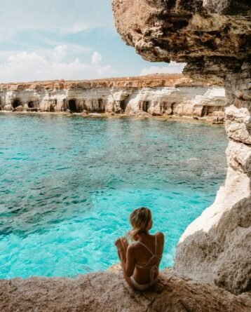 Woman sitting on a rocky cliff overlooking crystal-clear blue waters in Paphos, Cyprus
