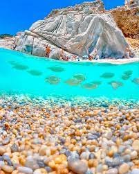 Crystal-clear waters and scenic beach in Ikaria, Greece, with underwater pebbles and rocky cliffs